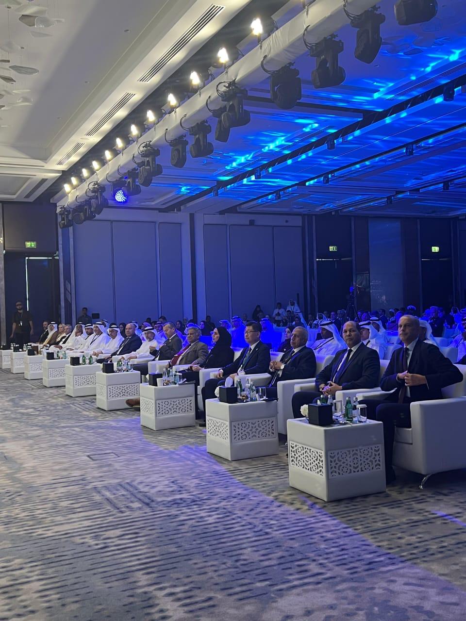 Officials and delegates seated in the forum ballroom under blue stage lighting
